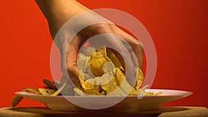 Womans hand grabbing chips from plate, home party with junk food, slow motion