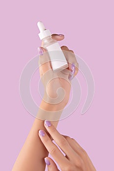 Womans hand holding dropper with serum on pastel lavender background