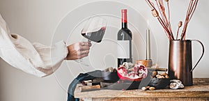 Womans hand holding glass of wine and snacks, wide composition