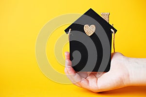 Womans hand holding little toy house made of chalk board on a orange background