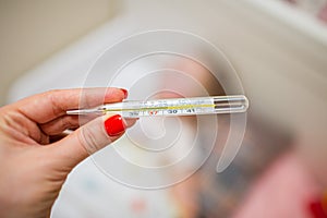 Womans hand holding mercury thermometer on the background of a sick child