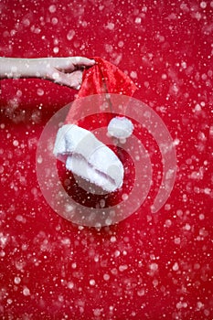 Womans hand holding a Santa Claus hut on red background with sno