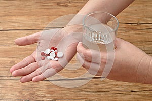 A womans hand holding a variety of small red and white pills and a glass of water