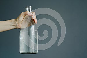 Womans hand holds bottle with water on gray wall background