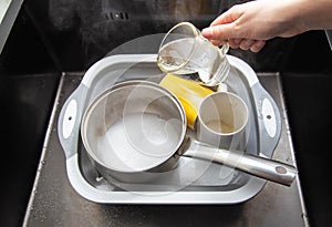 A womans hand pours hot water into a basin with dirty dishes and environmentally friendly oxygen bleach. Washing