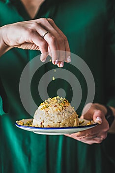 Womans hand puring pistachio nuts to sweet semolina helva