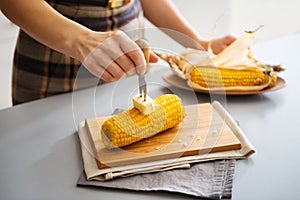 A womans hand putting butter on corn on the cob on board