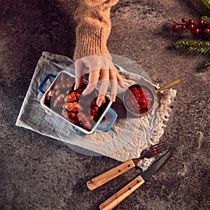 Womans Hand Reaches For Dish Of Traditional Christmas Pigs In Blankets On Table Set For Meal