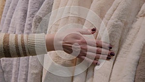 Womans hand touching luxury faux fur winter jackets for winter sale on a clothes rack in a retail fashion store