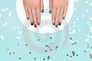 Womans hands with black manicure on silver circle and pastel blue background.