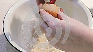 Womans hands broking yellow egg in bowl with ingredients for dough.