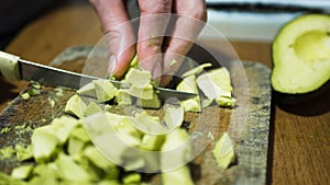 Womans hands cutting avocado on board, sliced and whole avocadoes bowl over wooden background. home cuisine