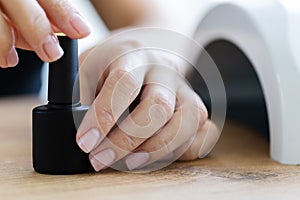 Womans hands holding black bottle of shellac. Manicure concept.