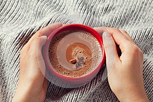 Womans hands holding a cup of hot cocoa or hot chocolate on knitted background, traditional beverage for winter time