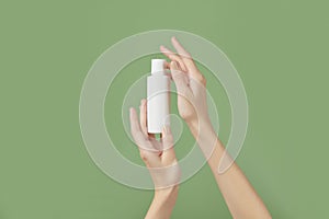 A womans hands holding a white cosmetic bottle on a green background