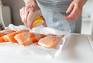 Womans hands pouring or sprinkling lemon juice on a raw salmon fillet