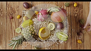 Womans hands put fresh ripe organic tropical fruits into box with wood shaving on a wooden background. Top view. Fast