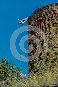 Womans legs kicking out into the air from top of ancient castle wall - weeds out of focus in foreground - Tbilisi Georgia