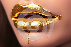 A womans mouth in close up with a liquid golden make up