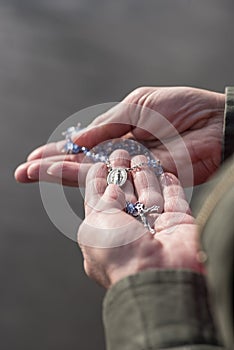 Womans open hands holding a beautiful rosary with blue beads and praying