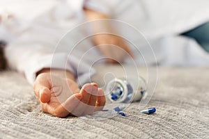 Womanâ€™s hand close up committing suicide by overdosing on medication, pills and bottle beside. Overdose pills and addict concept