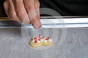 Womanâ€™s hand dropping sugar sprinkles onto a heart shaped frosted sugar cookie