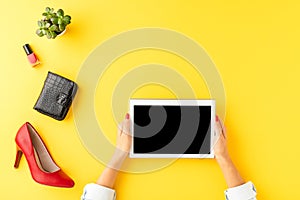 Womanâ€™s hand holding digital tablet with empty screen on background with high heels and fashionable accessories.