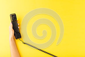 Womanâ€™s hand holding vintage handset on yellow background. Customer support concept