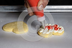 Womanâ€™s hand piping red frosting onto a heart shaped sugar cookie