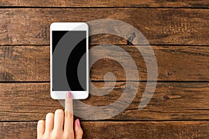 Womanâ€™s hand using smart phone with empty screen on rustic wooden background.