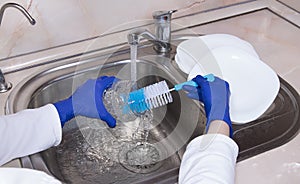 Womanâ€™s hands with blue gloves washing glass jar at kitchen faucet over the metal sink. Close up of hand with dish brush and