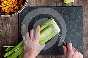Womanâ€™s hands cutting a bunch of celery, black cutting board and chef knife