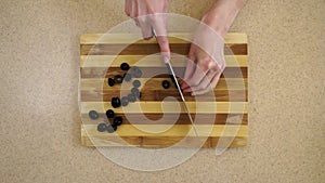 Womanâ€™s hands are cutting olives on a kitchen board by a metal knife. a view from the top