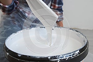 Womanâ€™s hands mixing a gallon of grey paint with wooden paint stirring stick.