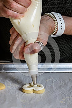 Womanâ€™s hands piping vanilla frosting onto a heart shaped sugar cookie