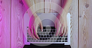 Womanâ€™s hands typing on laptop keyboard in purple light. View from above. Remote work concept image. 4K video