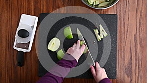 Womanâ€™s hands using a chef knife to cut the core out of granny smith apple quarters