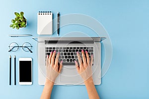 Womanâ€™s hands using laptop on blue table with accessories. Business background with copyspace.