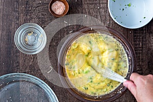 Womanâ€™s hands whisking raw egg mixture with chopped broccoli in glass bowl, on a wood table