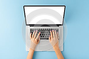 Womanâ€™s hands working on laptop with empty screen on blue background. Office desktop.