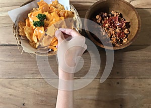 Womanâ€™s picking Nachos with cheese and Bali style dip on wooden table