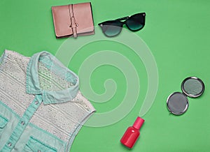 Women accessories and clothing on a green background. Jeans shirt, mirror, perfume bottle, sunglasses, purse. Copy space. Flat