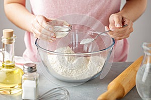 Women adds the baking powder into the glass bowl with flour.