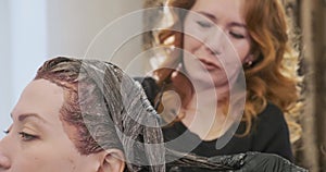 Women apply hair bleach on beauty salon visitor head closeup