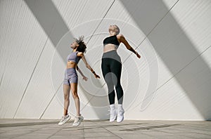 Women athlete in sportswear leaping in air with wall backdrop outdoors. Healthy lifestyle concept