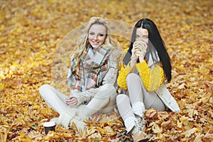 Women in autumn park drink coffee