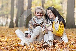 Women in autumn park drink coffee