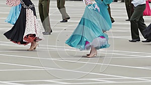 Women in ball gowns and men in military uniforms dance on asphalt parade ground.