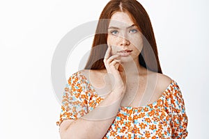 Women beauty and skin care. Young timid girl with red hair, touching her face and gazing sensual at camera, standing in