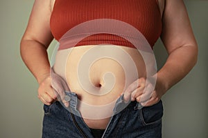 Women body fat belly. Obese woman hand holding excessive belly fat. Fat woman trying to zip up her jeans pants
